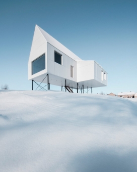 魁北克白雪皑皑的休息室-白色的混凝土和金属波纹板组成外表面，一个清晰的轮廓字形，里面有暖炉的户外生活空间