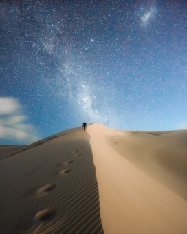 夜空下行走的沙丘上的旅行者