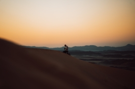 手拿数码相机跪在沙漠上查看片子的摄影师