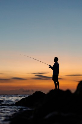黄昏海岸礁石上垂钓人物剪影氛围感摄影